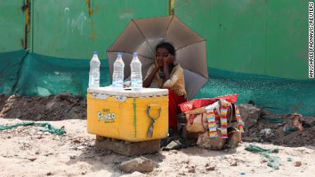 ニューデリーでは、水を売っている女の子が傘を使って太陽光線から身を守っています。