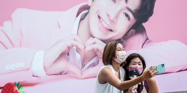 2人の女性が看板の前で自分撮りをし、ボーイグループCantopopのメンバーであるAnsonLuの写真を見せています。 "鏡、" 香港で。